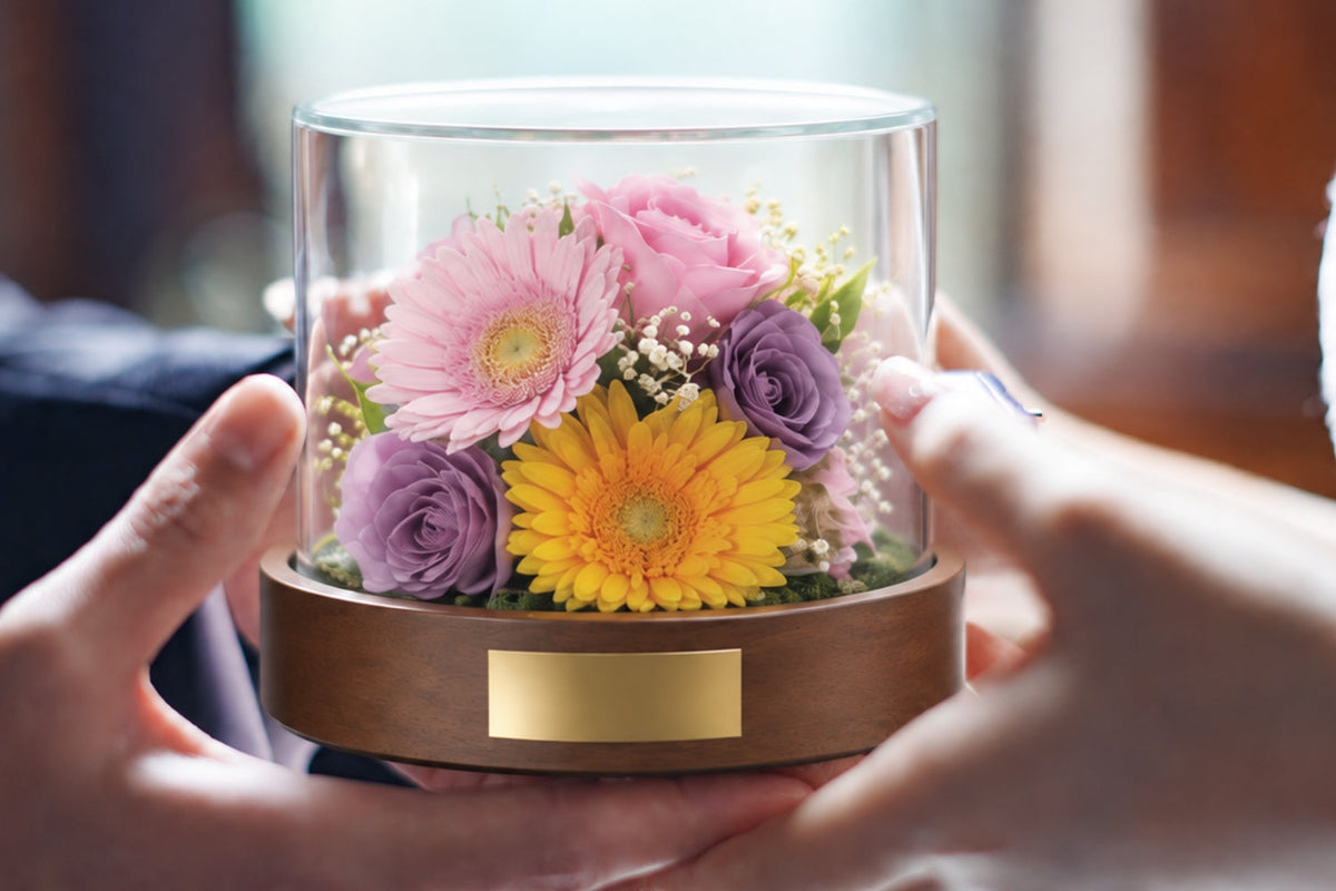 パステルカラーの花をガラスドームに収めたKoronを両手で持つ